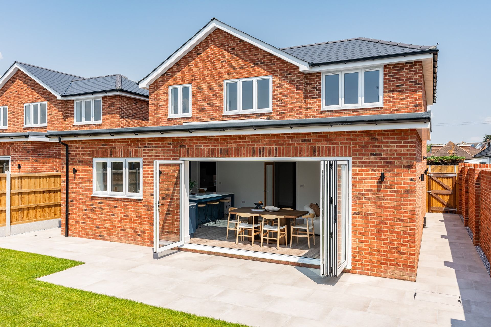 The back of a finished Branksome Avenue home, its bi-fold doors folded open to the dining room and patio.